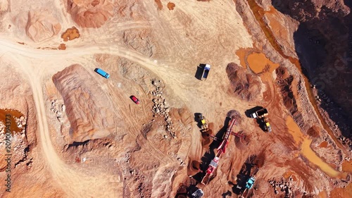 Quarry trucks and crusher machinery, Bulgaria. Overhead view of colorful vehicles on red dirt roads beside orange mineral ponds.