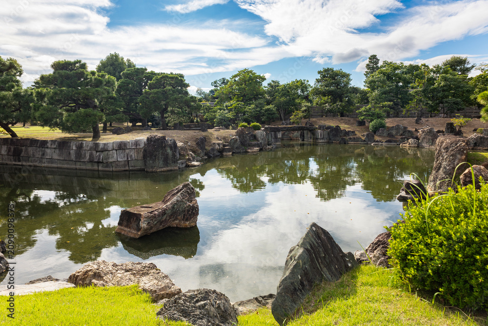 Fototapeta premium Japanese garden scenery at Nijo Castle Kyoto featuring calm water manicured greenery and historic palace building, Kyoto, Japan 