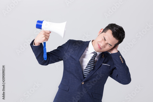 Tableau sur toile Frustrated businessman covering ear while holding megaphone