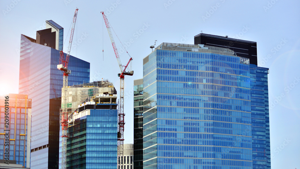 Fototapeta premium Crane on the construction site in a site surrounded by the high buildings. Office building under construction in the vicinity of high apartment buildings and office building.