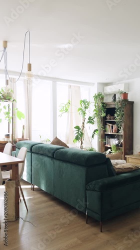 Modern and stylish living room interior with a large green velvet sofa. Comfortable apartment filled with natural light and many plants