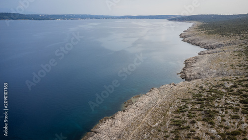 Konstfotografi Elevated aerial view of rocky coastline beside calm blue sea with distant shorel