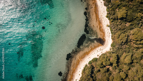 Foto Aerial view of turquoise sea meeting rocky sandy shoreline beside dense green co