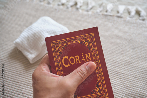 Person holding coran, a religious holy book text, over a prayer mat