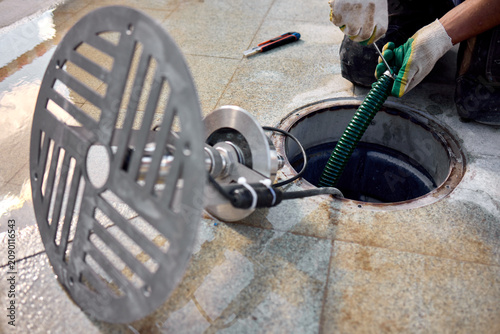 removal of manhole cover on sidewalk with concrete and metal materials, practical ground-level view, gray and green tones, utility maintenance in construction setting.
