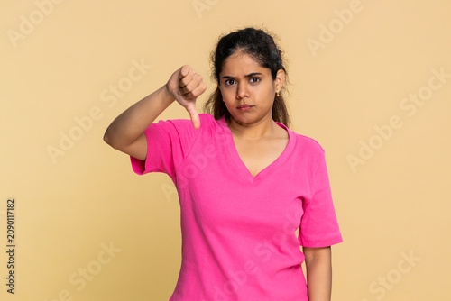 Fotografie Indian woman lightly shakes head with clear disappointment, lowers shoulders shows thumbs down