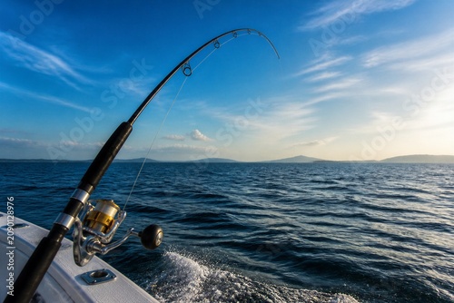 Fishing rod bending over side of fishing boat on open sea