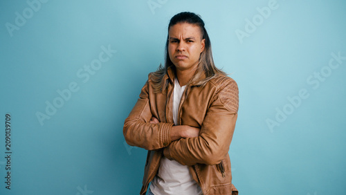 Konstfotografi Latino man with long hair standing crossing arms, looking at camera with a skept