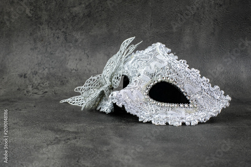 A silver lace masquerade mask with butterfly detail lies sideways on a dark grey textured surface. Suitable for carnival party, masquerade costume, Halloween accessory, mystery