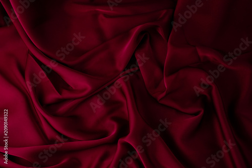 Dark red satin fabric creates deep folds and shadowed texture across the frame. Suitable for dramatic fabric background, luxury textile, product backdrop
