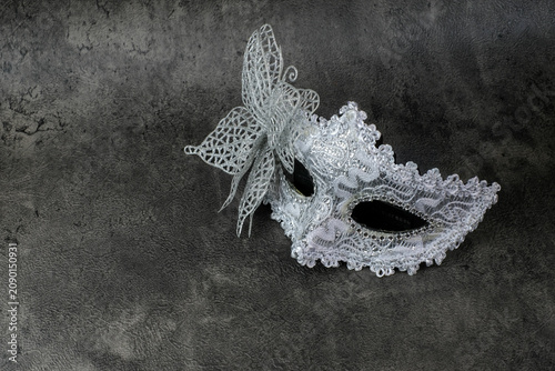 A silver masquerade mask with lace butterfly decoration is arranged on a dark grey textured background. Suitable for carnival mask, Halloween costume, masquerade party, theatrical accessory