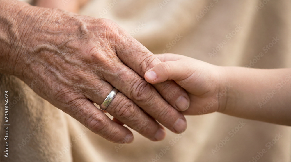 Fototapeta premium Elderly woman holding hand of small child. Generational connection and support. Concept of family love, care and legacy. Bond between aging grandmother and kid for social healthcare.