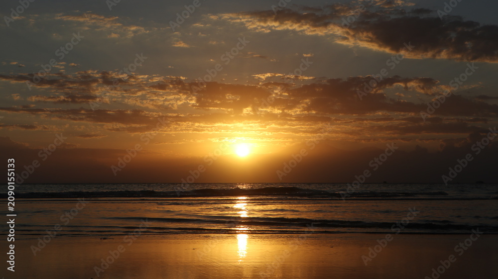Obraz premium Golden Coastal Sunset: The sun glows intensely as it sinks toward the horizon, casting a shimmering reflection across the calm ocean waves in the background