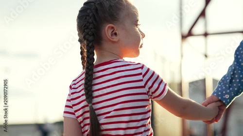 Confident adorable baby girl walking outdoor summer park sky with mother holding hands closeup back view. Cute female kid child enjoy happy childhood relaxing outdoor at bright sun sunrise sunset