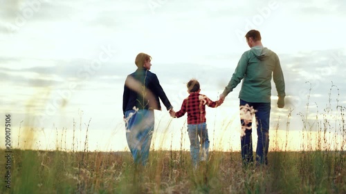 Small family enjoys leisurely walk in field basking in joyous moments brought by windy weather on holiday. Family hold hands walking across grassy valley. Family vacation and active pastime
