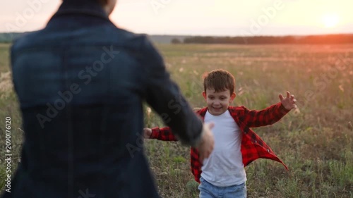 Joyful boy runs into tight hugs with mother standing in field in sunny weather. Boy and mother hug enjoying moment in evening. Mother and boy spend time in nature hugging on meadow