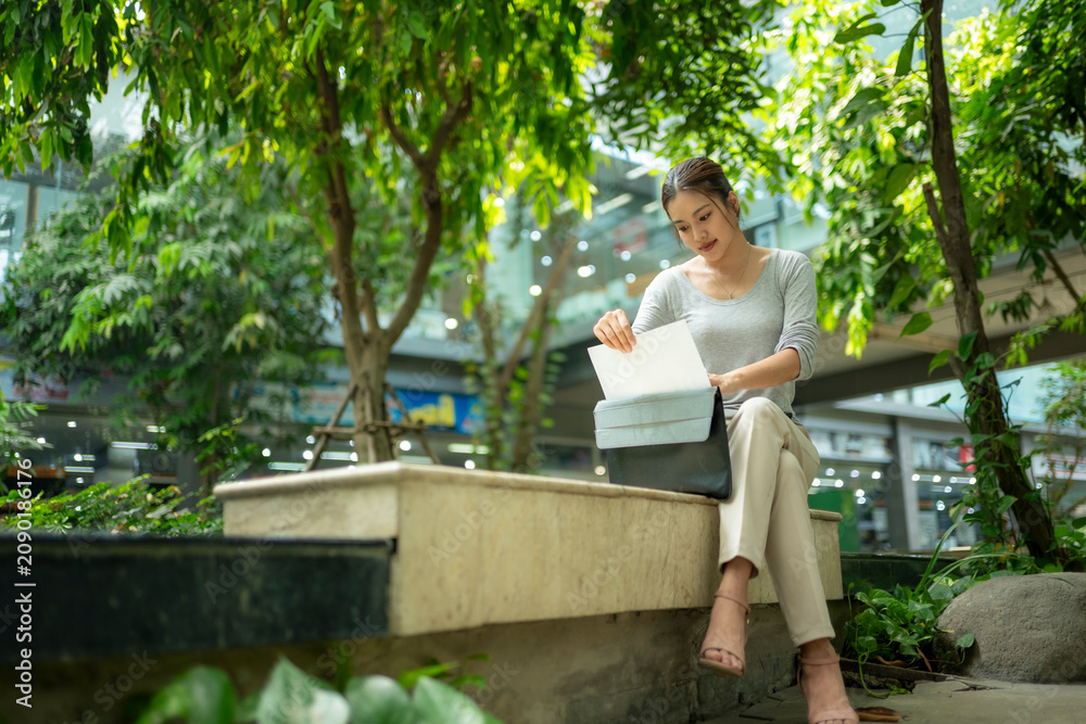 Fototapeta premium Woman Working Outdoors with Laptop Amid Lush Greenery in Urban Space