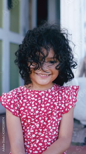 Portrait of a joyful Hispanic girl with beautiful curly hair smiling happily. Genuine childhood emotion and sincere expression outdoors. Vertical