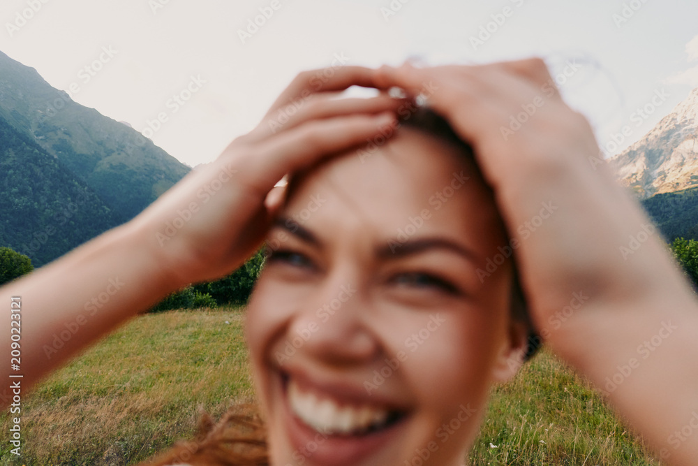 Fototapeta premium Smiling woman outdoors in a grassy field with mountains in the background, casual lifestyle, wellness vibe, natural light, cheerful candid moment and carefree energy.