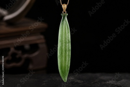 A slender green jade pendant shaped like a silique on a dark background.