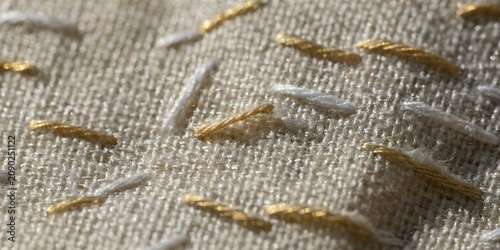 Extreme close up of antique embroidery stitching on linen filling entire frame, delicate thread detail muted gold and white tones