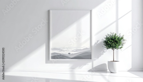 A minimalist interior scene features a framed landscape artwork and a potted plant illuminated by soft natural light casting shadows on a white wall.