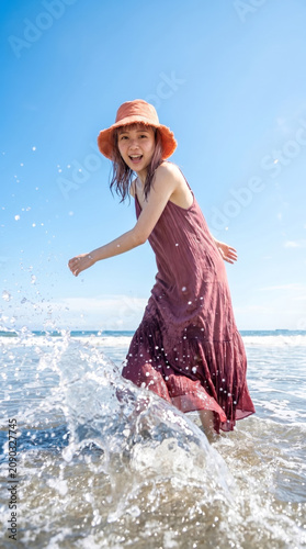 Tapety artystyczne 楽しそうに海の水を蹴り上げて水飛沫を飛ばす活発的な若い女性