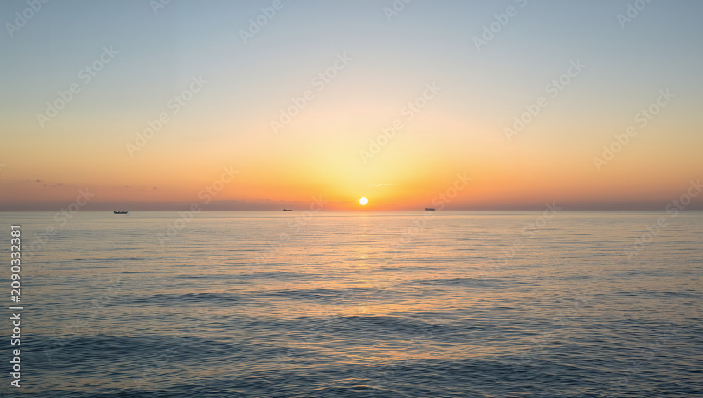 Obraz premium 朝焼けの太陽が穏やかな海に光を広げる風景