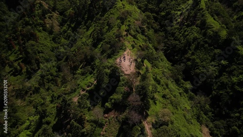 4k aerial drone video footage of Mount Merapi volcano seen from Klangon Hills emitting volcanic smoke from its summit crater, surrounded by forest mountain ridges, clear blue daytime sky.