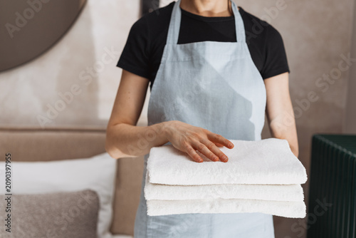 Maid holds fresh folded towels in hotel room during cleaning service