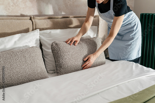 Woman making a bed in a hotel room during cleaning service