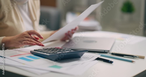 Close-up of Asian businesswoman hand using calculator and holding financial document for budget planning at home.
