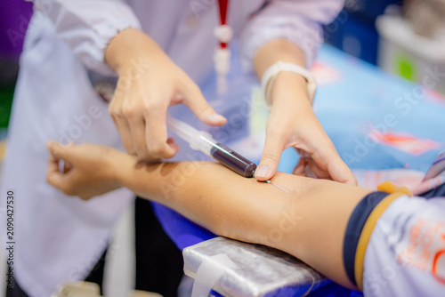 Medical professional collecting a blood sample from a patient's arm using a syringe during a healthcare examination. Close-up of venipuncture procedure in a clinical environment with selective focus a