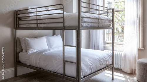 Bedroom interior featuring a dark metal frame bunk bed with clean white bedding and natural window light.
