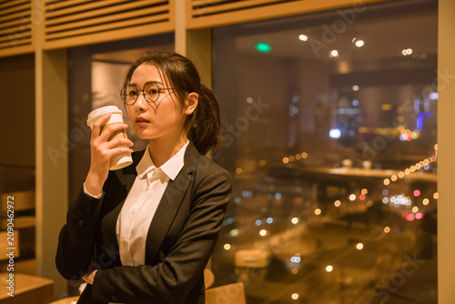 Thoughtful young businesswoman with takeaway coffee in cafe at night