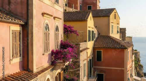 Ligurian street with colorful buildings, blooming flowers, and sea view.