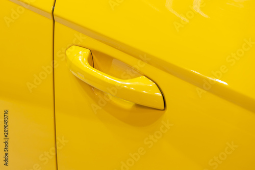 Close up of yellow car door handle and sleek automotive bodywork. Professional vehicle photography showcasing vibrant paint finish and modern transport design. Clean minimalist aesthetic