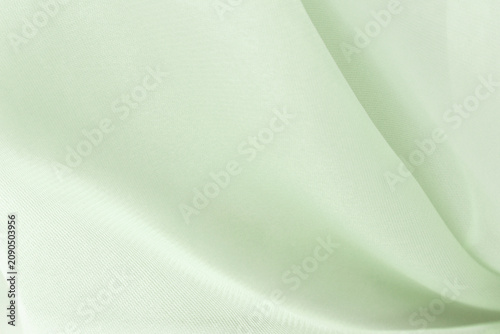 Soft delicate transparent organza, chiffon, silk fabric in soft sage green. Close up folds of fabric textile texture as background in pale green color with copy space.