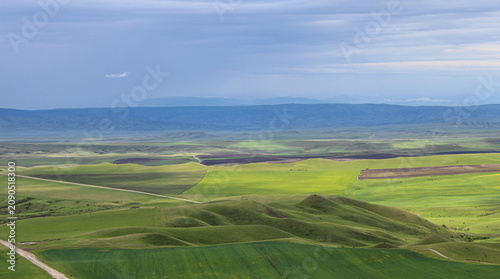 Aerial view of the Alazani Valley. Green hills and plowed fields. Caucasus Mountains and a cloudy sky in the background. Kakheti, Georgia