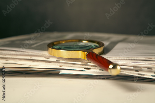 Magnifying glass and pile of newspapers on black background, closeup