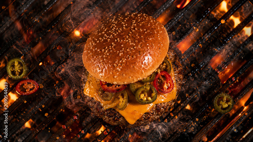 Delicious grilled hamburger with cheese and jalapenos, sizzling over an open flame, perfect for summer grilling.