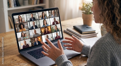 An over-the-shoulder view of a person gesturing with their hands while speaking during a video conference call with multiple participants on their laptop.