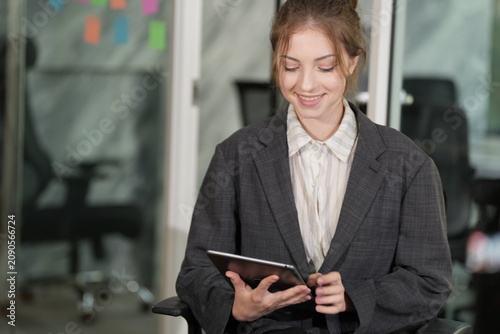 Fotografie Seated in a roomy gray blazer, the businesswoman reads her tablet with a soft smile, colorful sticky notes scattered across the glass wall behind her in a bright modern coworking office
