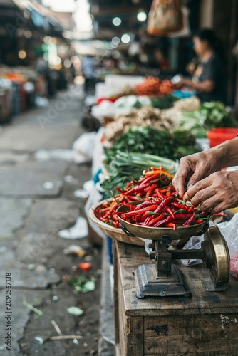 Weathered hands weighing fresh red chilies on traditional scale at Indonesian wet market at dawn