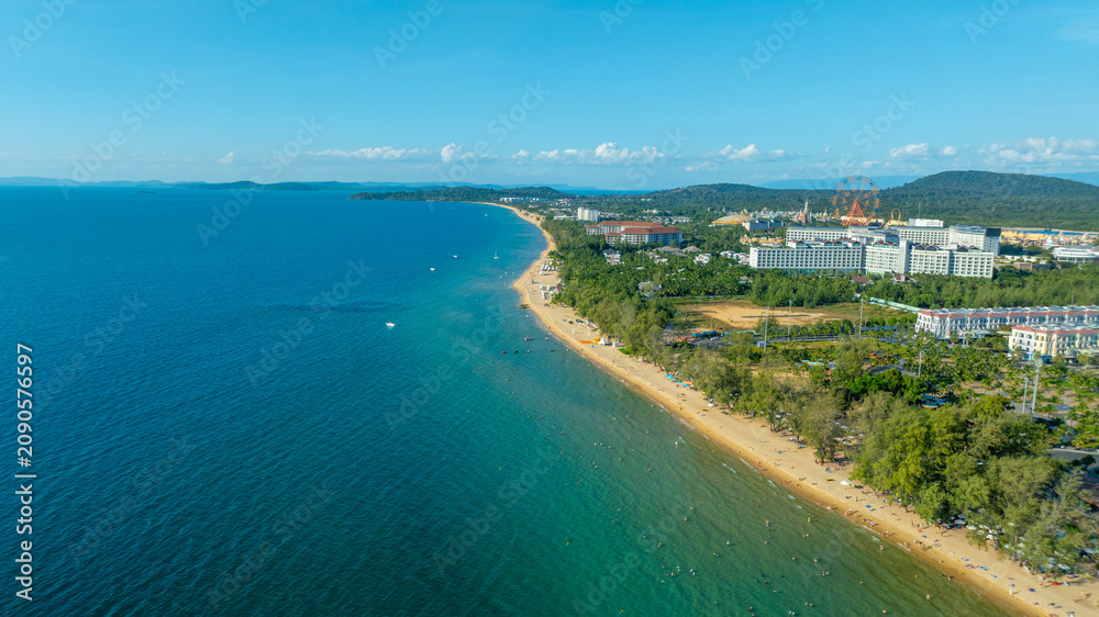 Fototapeta premium Aerial view of colorful mediterranean buildings along grand canal with pedestrian bridge. Grand world Phu Quoc with vibrant cafes, shops and blooming trees.