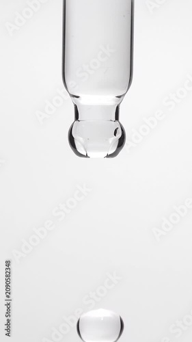 Macro shot of a pure micellar water or transparent salicylic acid serum droplet falling from a glass pipette dropper isolated on a solid white background