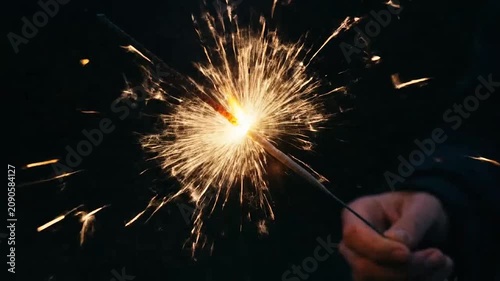 A hand holds a bright burning sparkler against a dark background