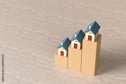 Small model houses sitting on ascending wooden block steps to represent rising home values and increasing real estate prices on a textured surface