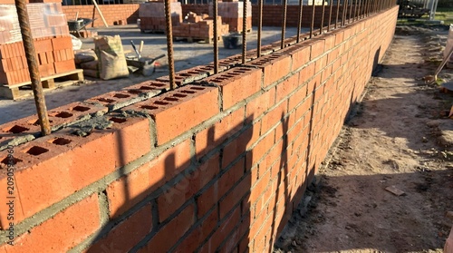 Red brick wall construction with steel rebar reinforcement, masonry work on a residential building site, industrial bricklaying process for house foundation