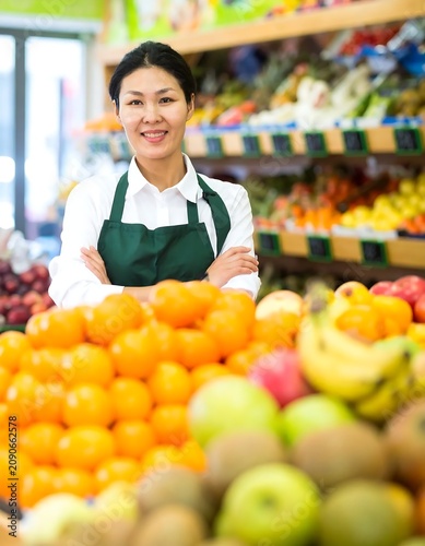 Smiling Female Grocer Standing with Folded Arms in Bright Produce Market